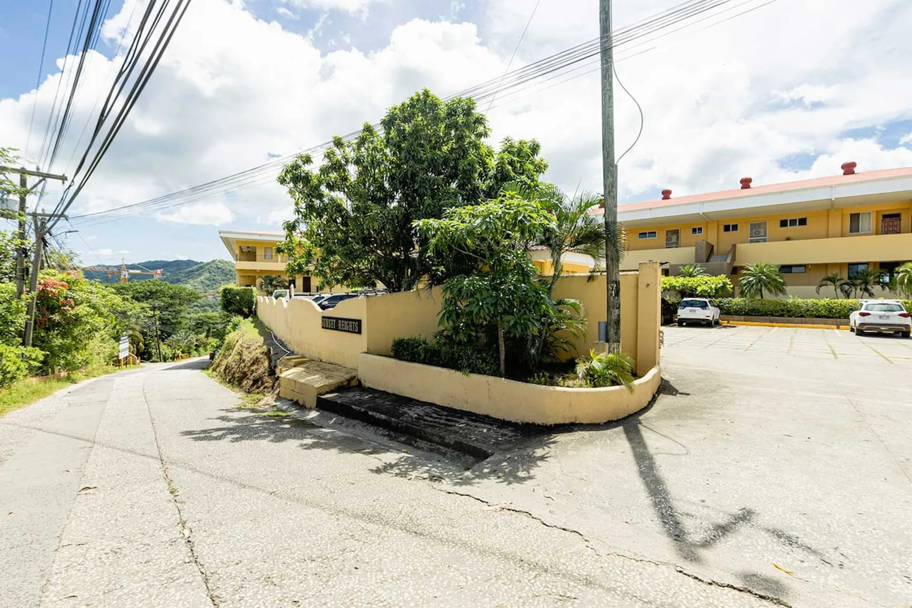 Shared amenity: A paved road curves past a landscaped entrance beside a yellow building.