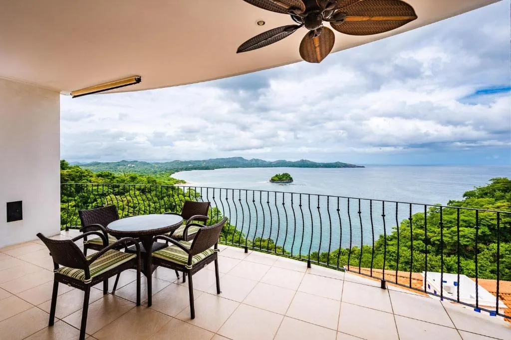 A balcony seating area overlooks the water and a small green island.