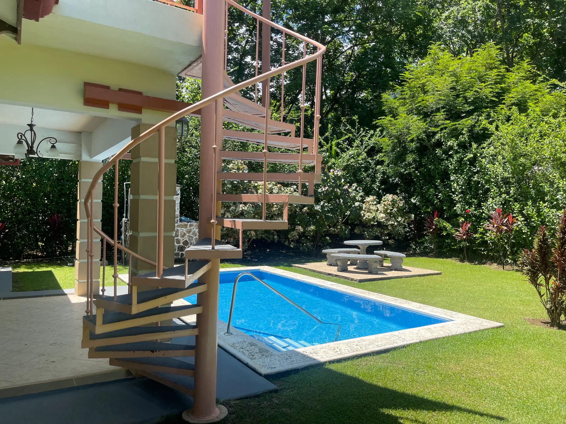 A swimming pool sits beside a spiral staircase and a small outdoor seating area.
