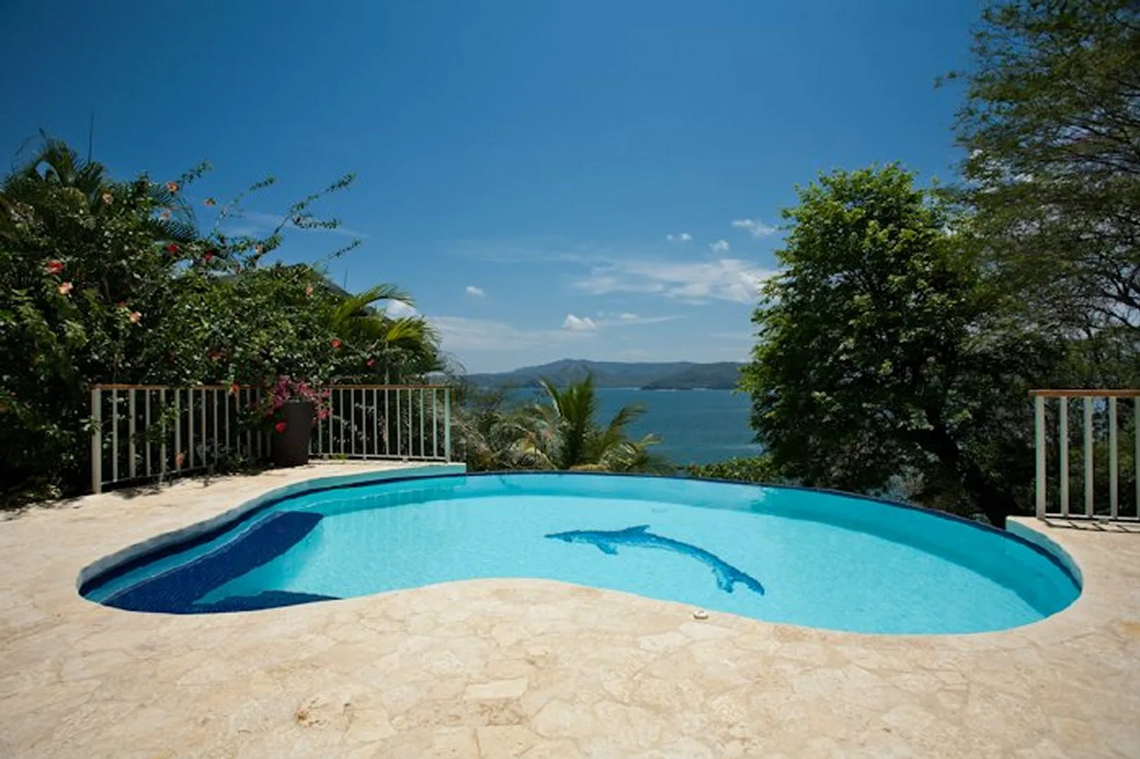A swimming pool overlooks the water, with trees and greenery around the patio.