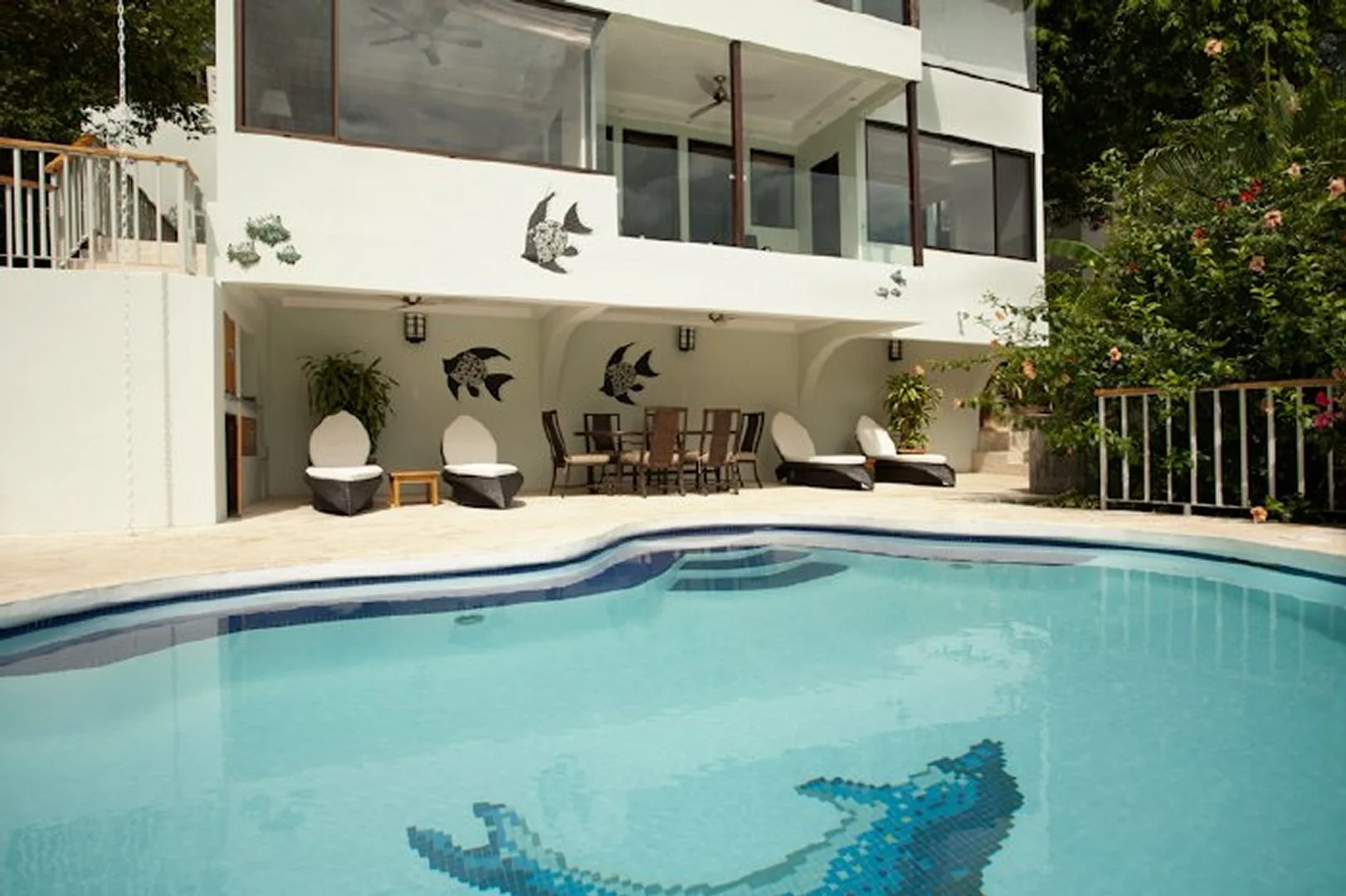 A swimming pool in front of a white building with patio seating.