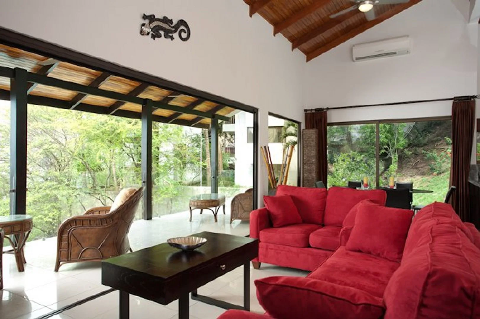 A living room with red seating beside large windows overlooking greenery.