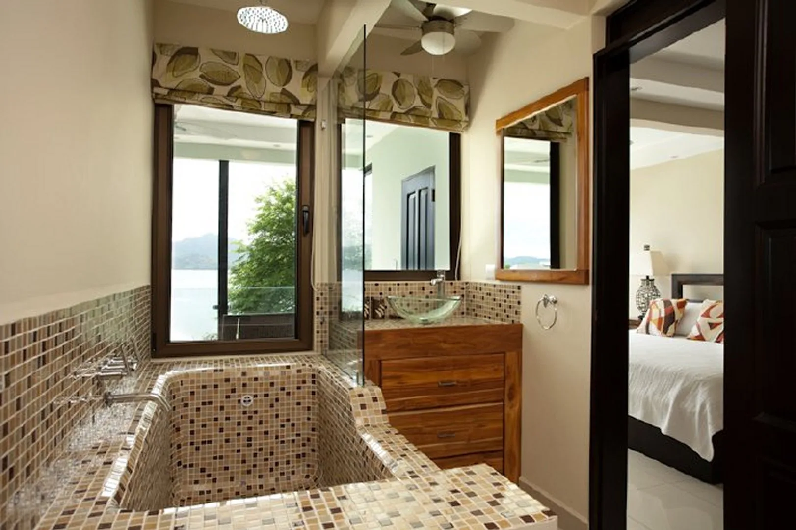 A tiled bathroom with a built-in bathtub, wooden vanity, and adjoining bedroom.