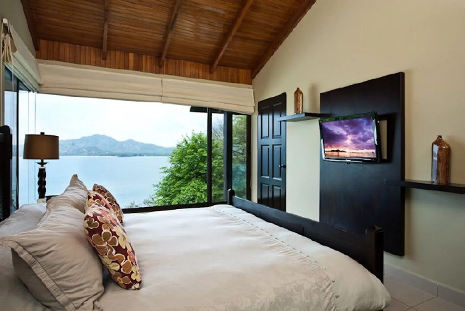 A bedroom with a bed facing a wall-mounted television and a lake view.