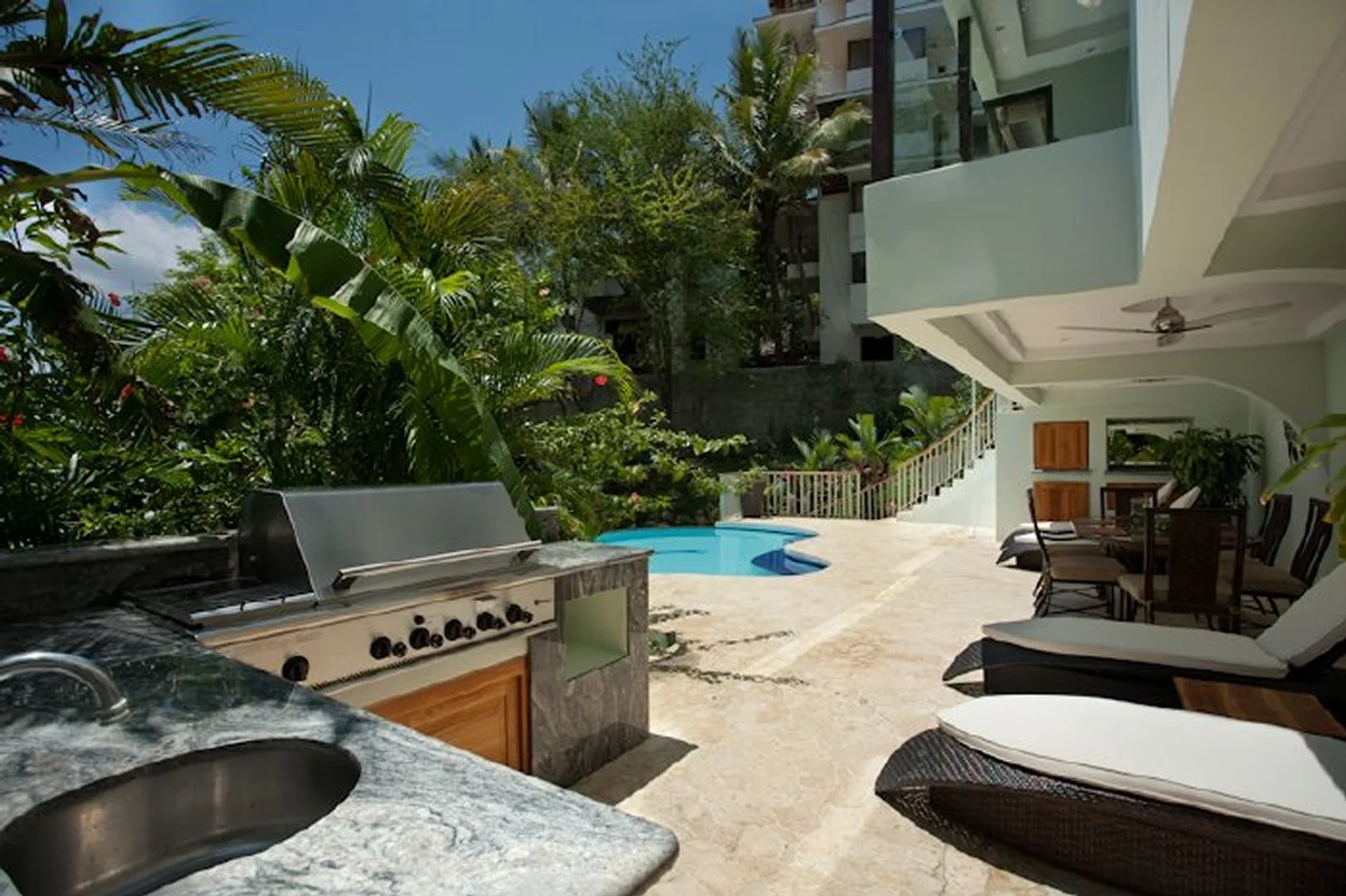 An outdoor patio with a built-in grill, seating, and a small pool.
