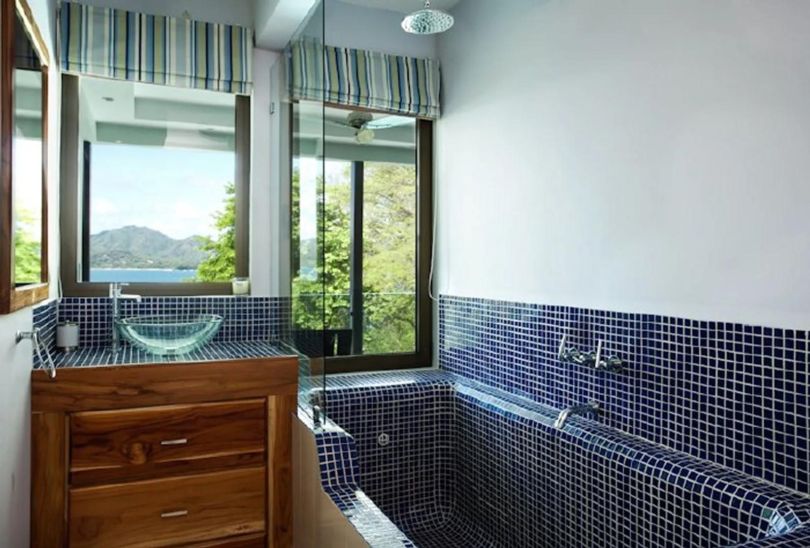 A tiled bathroom with a wooden vanity and a large window overlooking greenery.