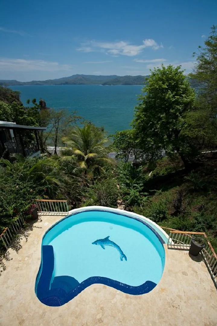 A small swimming pool overlooks a blue bay surrounded by green hills.