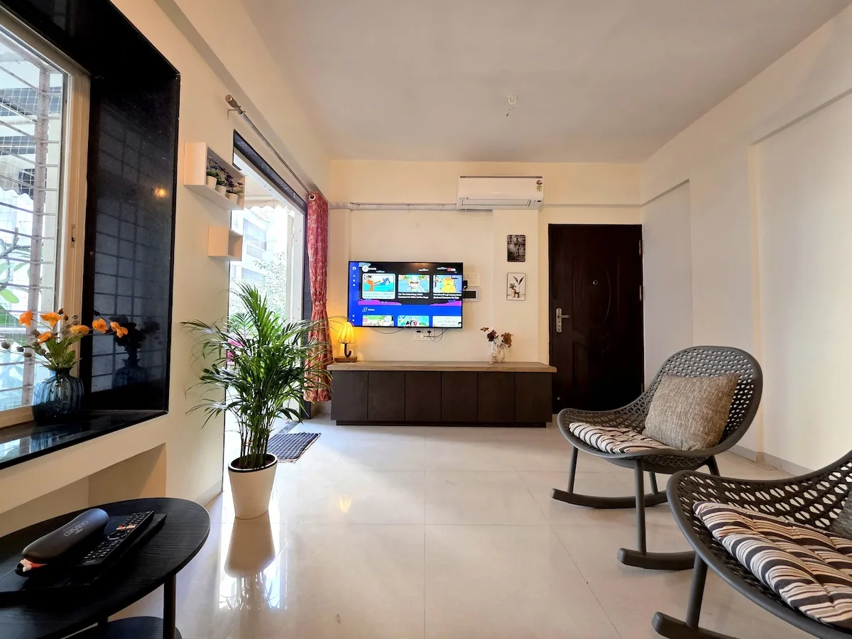 Una sala luminosa con un televisor montado en la pared y asientos tejidos.