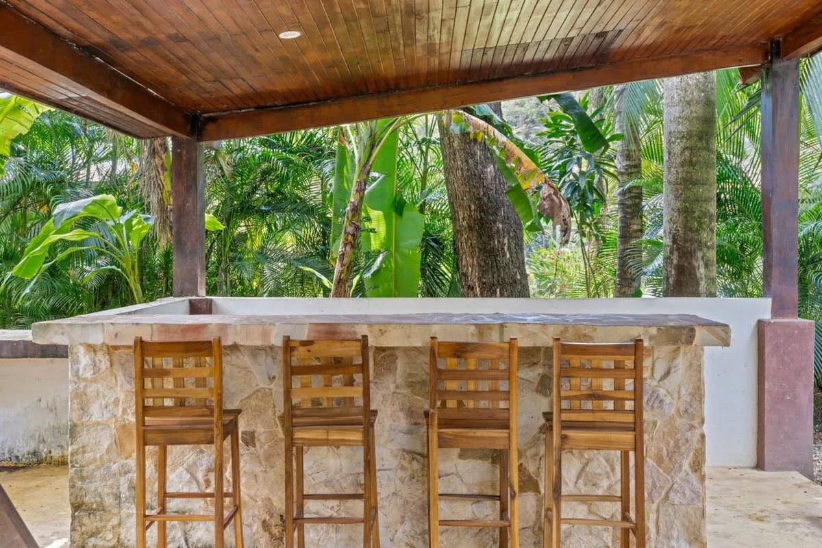 Una barra exterior techada con taburetes de madera da a una exuberante vegetación tropical.