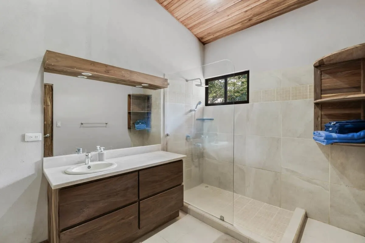 Un baño con tocador, espejo y ducha con mampara de vidrio.