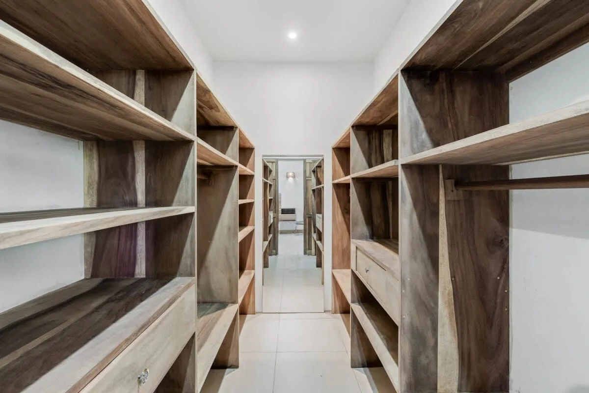 Un vestidor estrecho con estantes abiertos de madera y cajones.