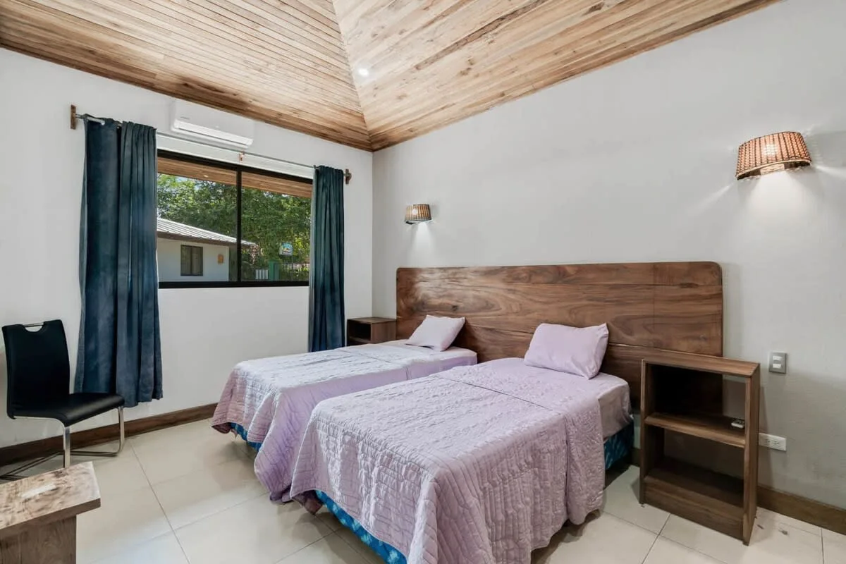 Un dormitorio con dos camas y una ventana con vistas a vegetación.