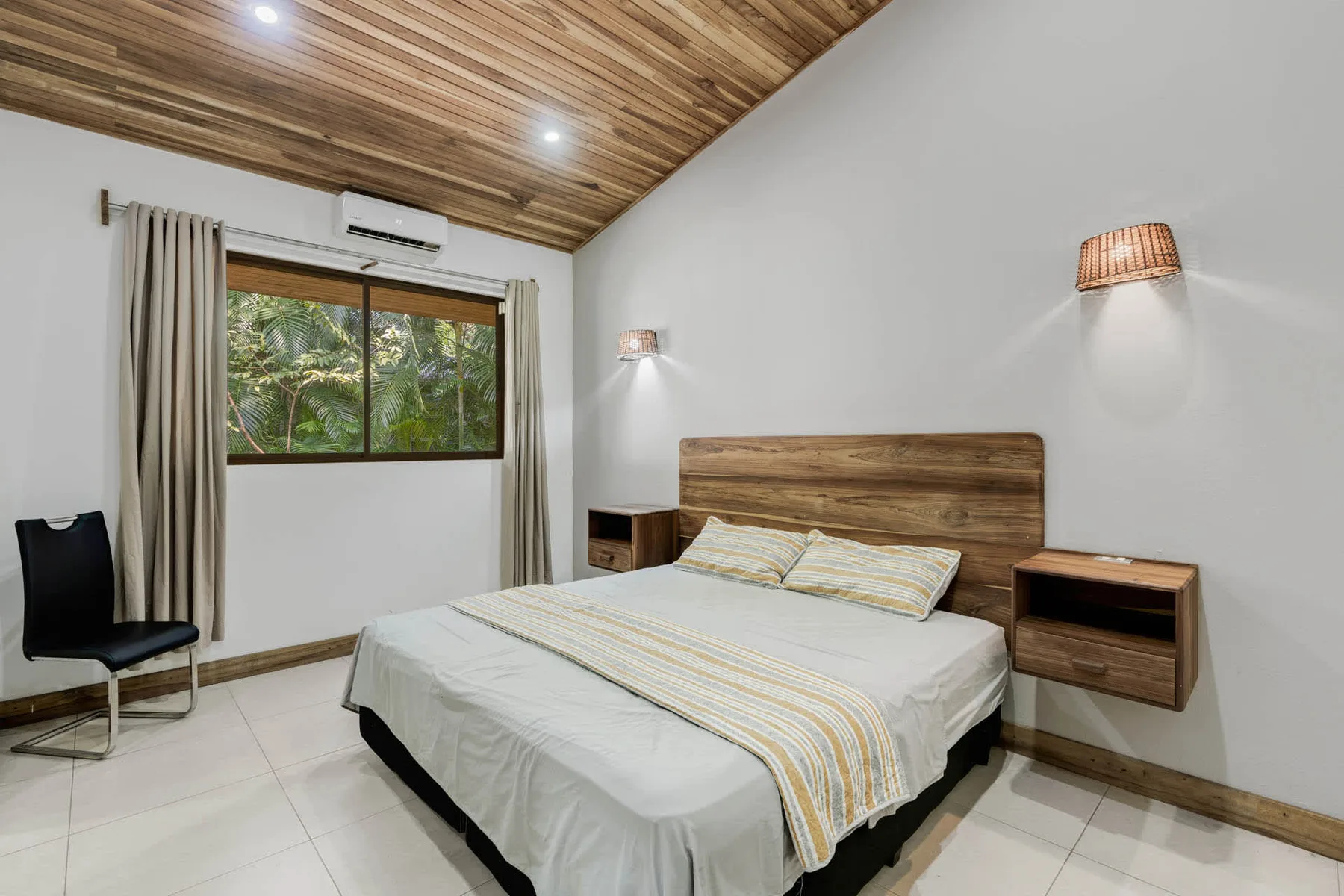 Un dormitorio con cama, techo revestido de madera y una ventana con vista a la vegetación.