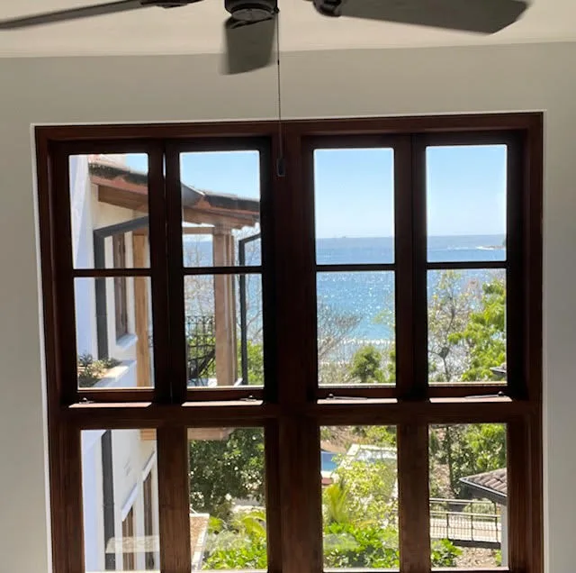 Una ventana grande da al océano y a la vegetación.
