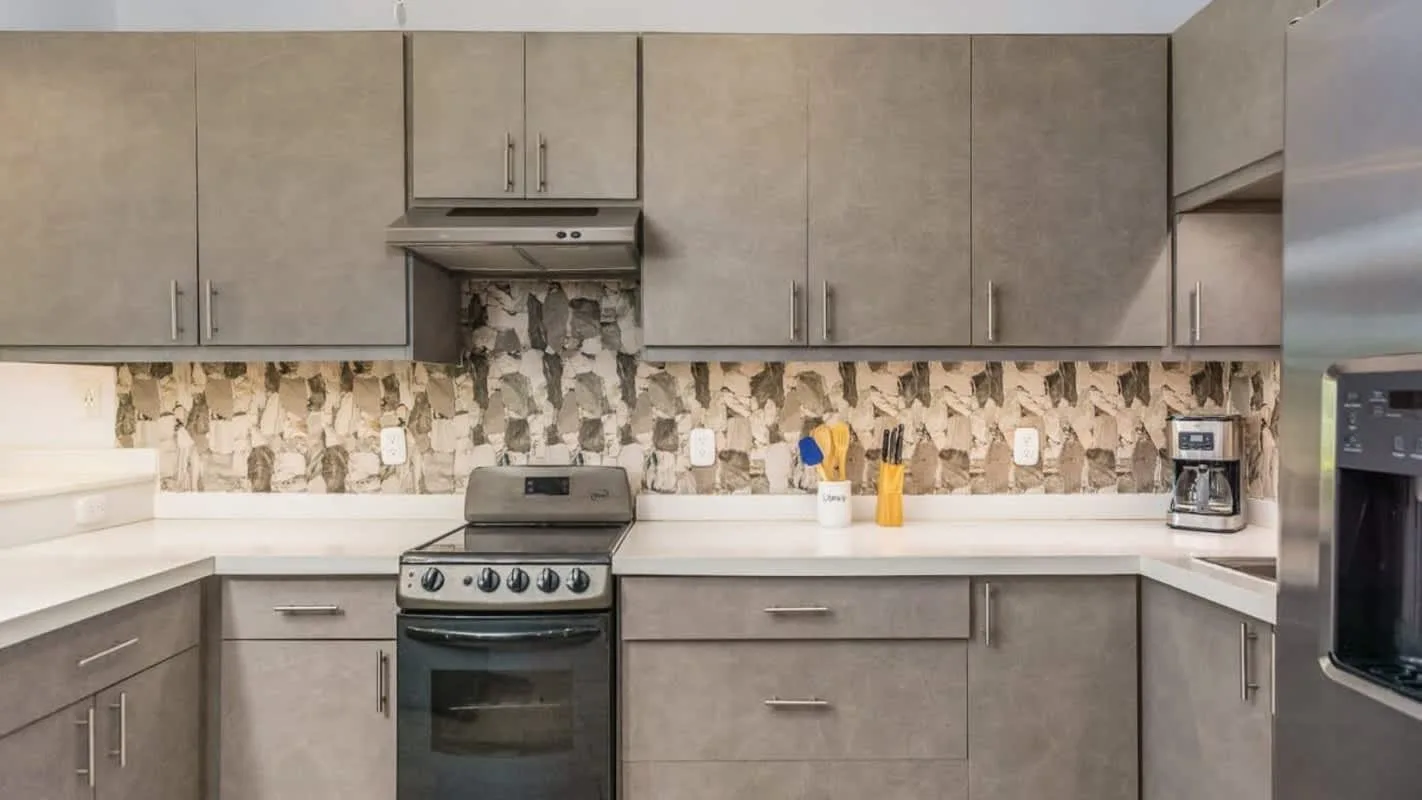 A kitchen with gray cabinets, a stove, and a patterned backsplash.
