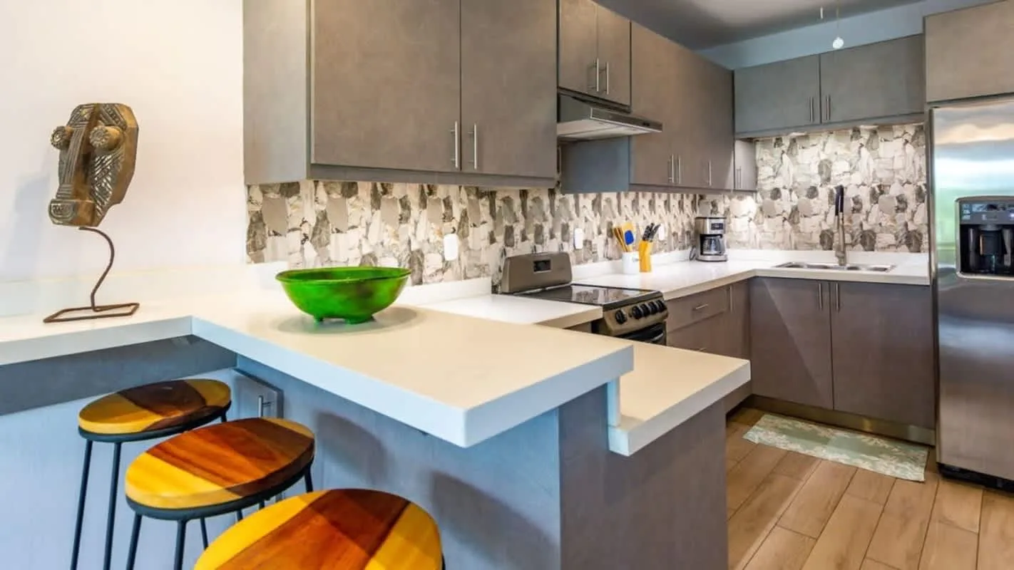 A modern kitchen with a counter, colorful stools, and stainless steel appliances.