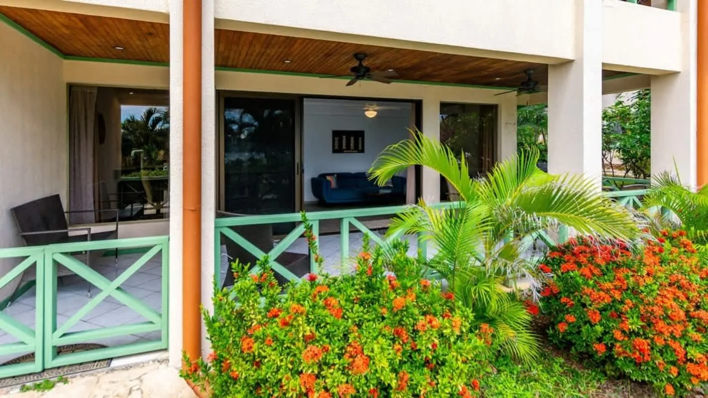 A covered patio overlooks colorful flowering shrubs and palm plants.