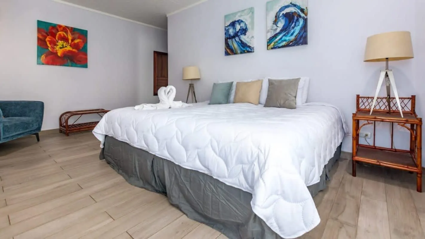 A bedroom with a large bed, colorful wall art, and wooden flooring.