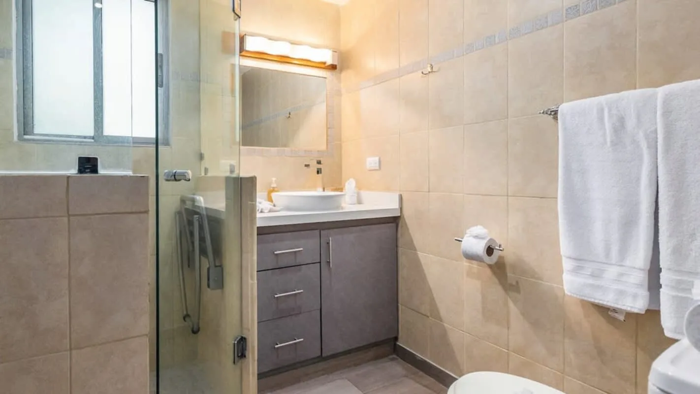 A tiled bathroom with a sink vanity, mirror, and glass shower.