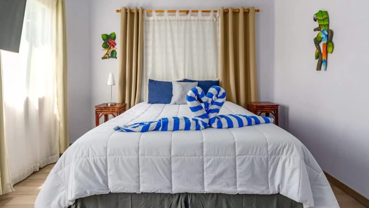A bedroom with a neatly made bed and blue-and-white striped towel decorations.