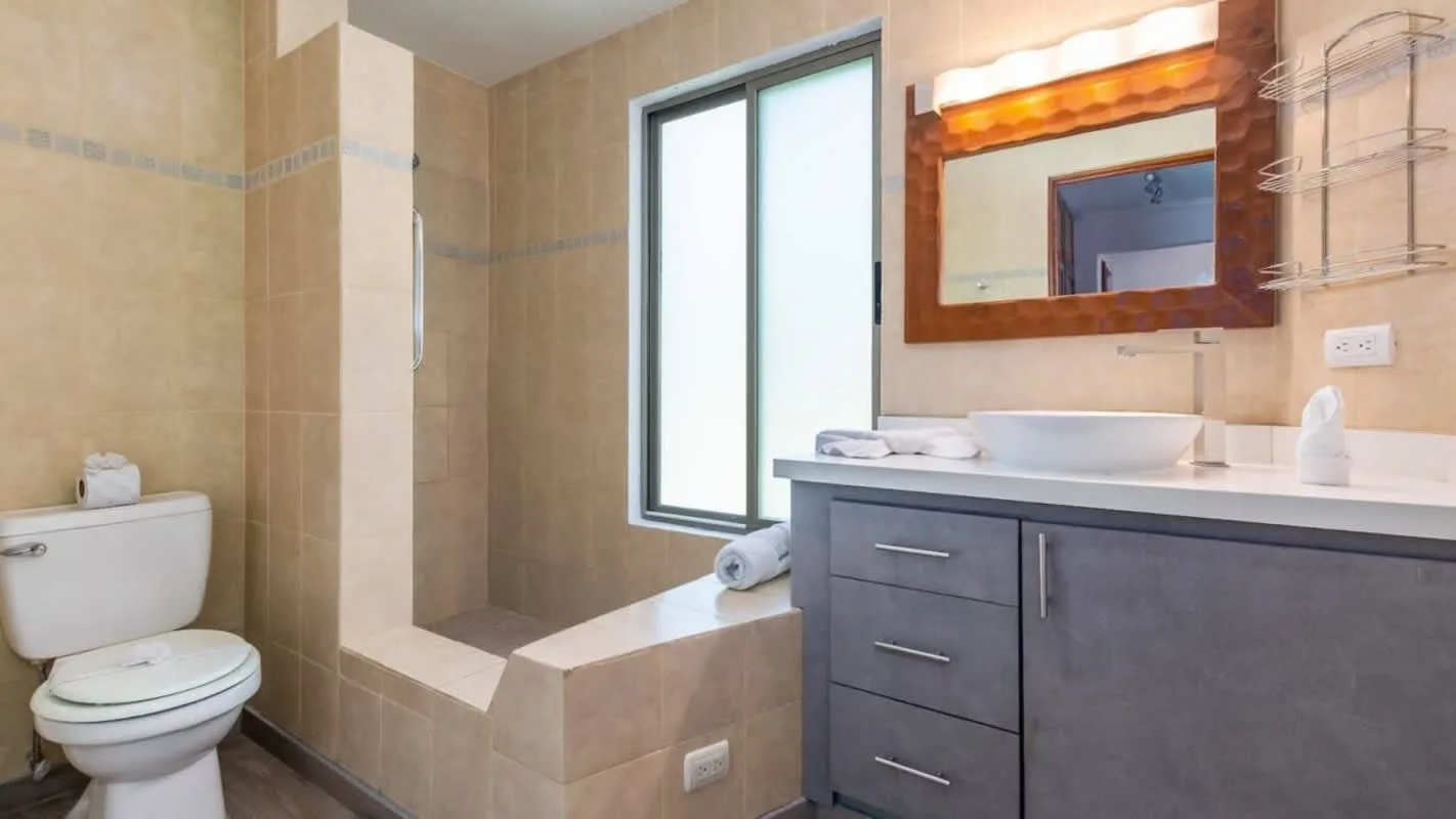 A tiled bathroom with a toilet, vanity, and large window.