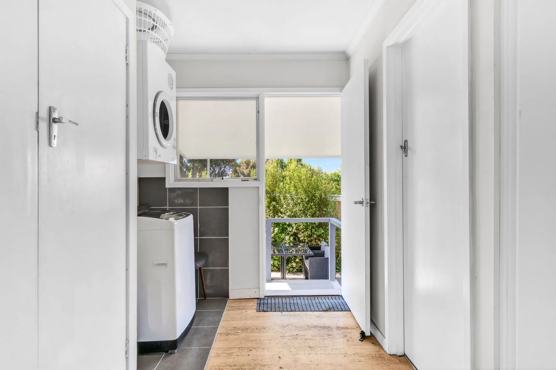 A bright laundry area opens onto a small balcony with greenery outside.