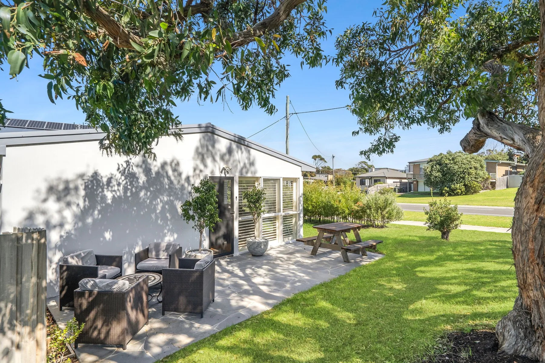 Outdoor patio seating beside a white building, with a picnic table on the lawn.