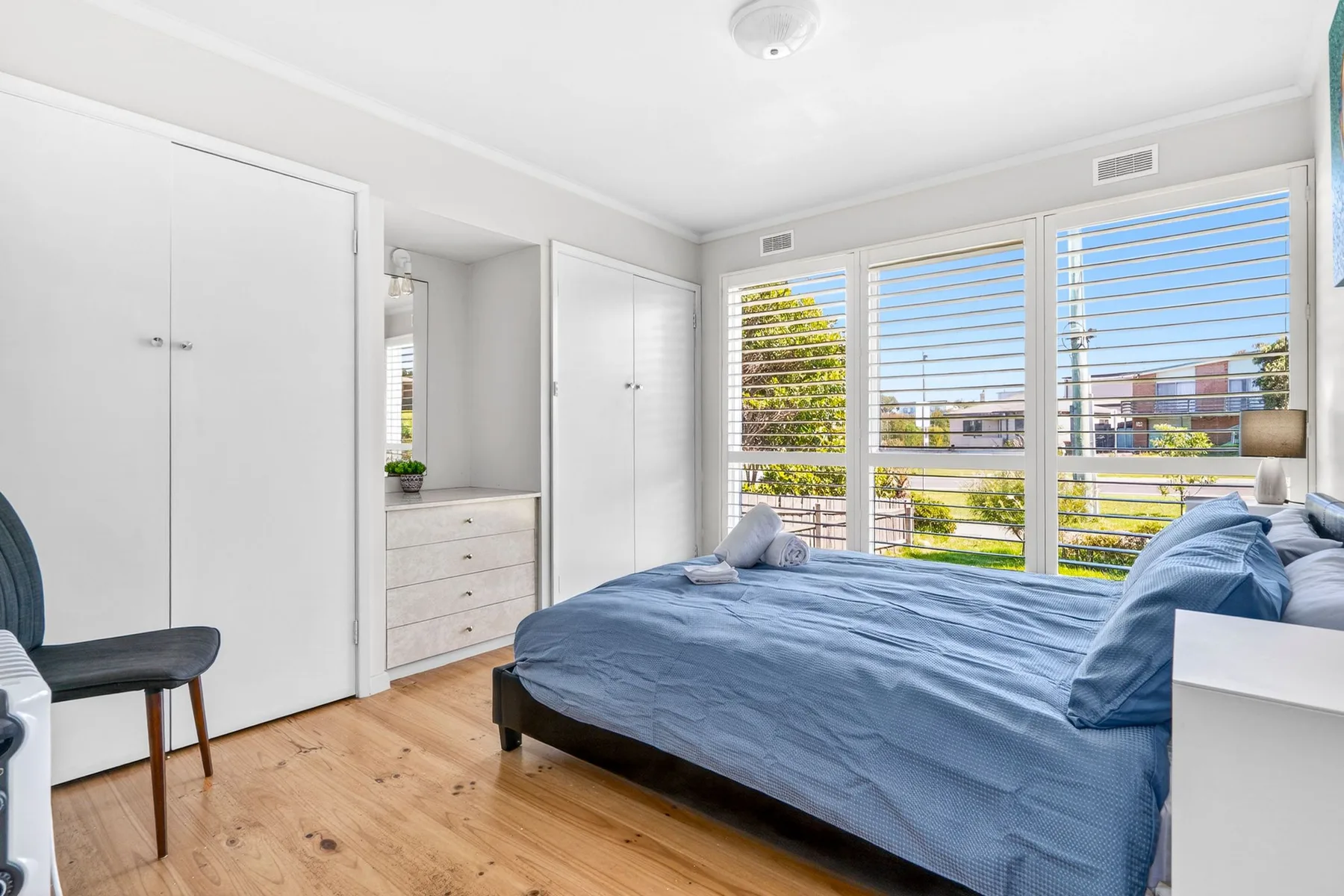 A bright bedroom with blue bedding and wide windows overlooking greenery.