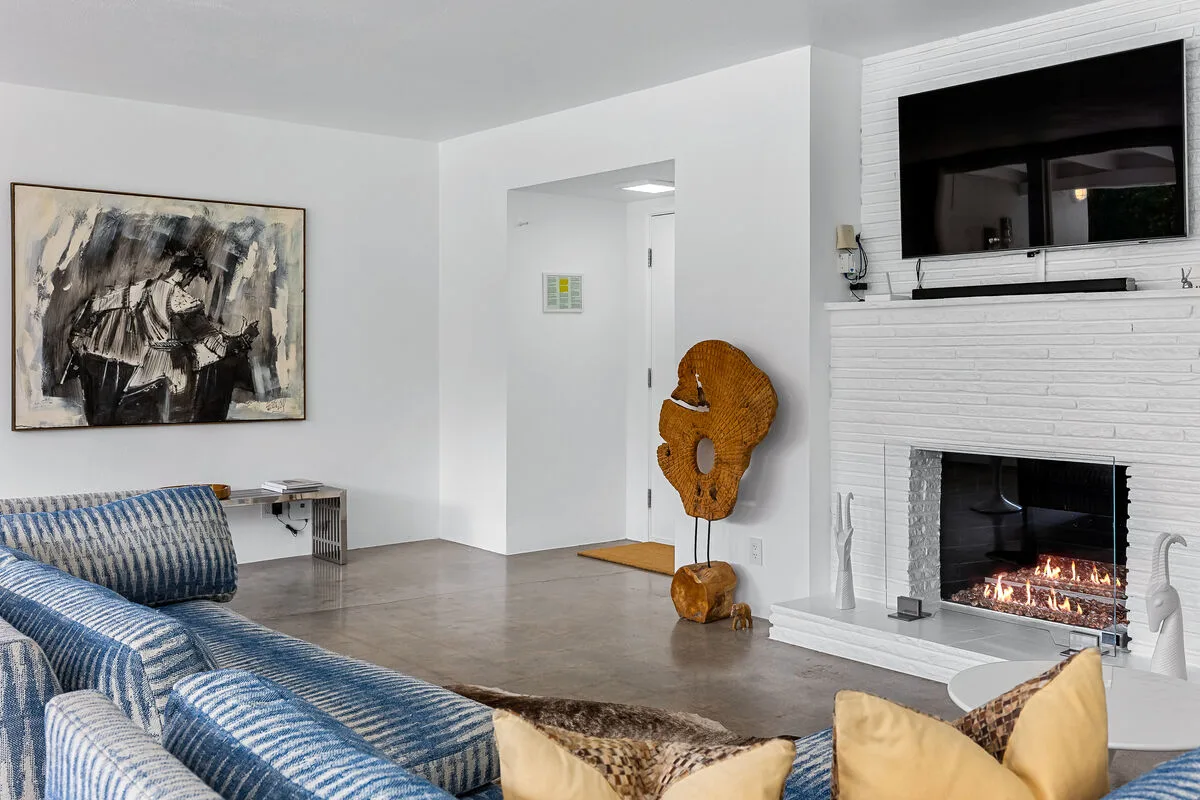 A bright living room with patterned seating and a fireplace beneath a wall-mounted television.