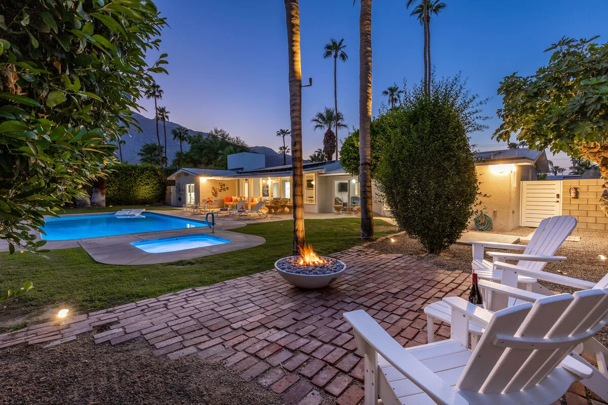 An outdoor patio overlooks a swimming pool, with seating and a lit fire feature.