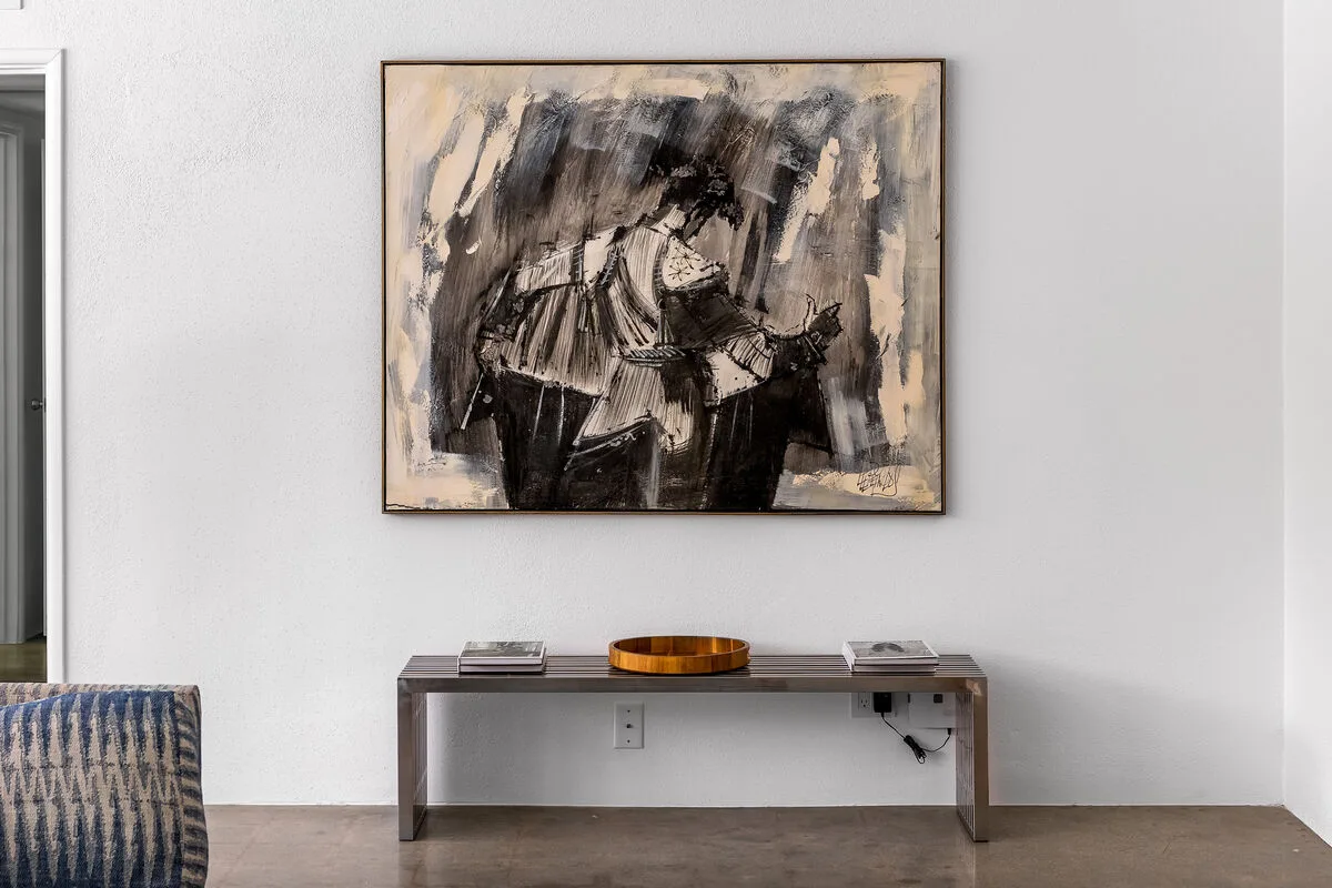 A console table sits beneath a large abstract painting in a bright room.