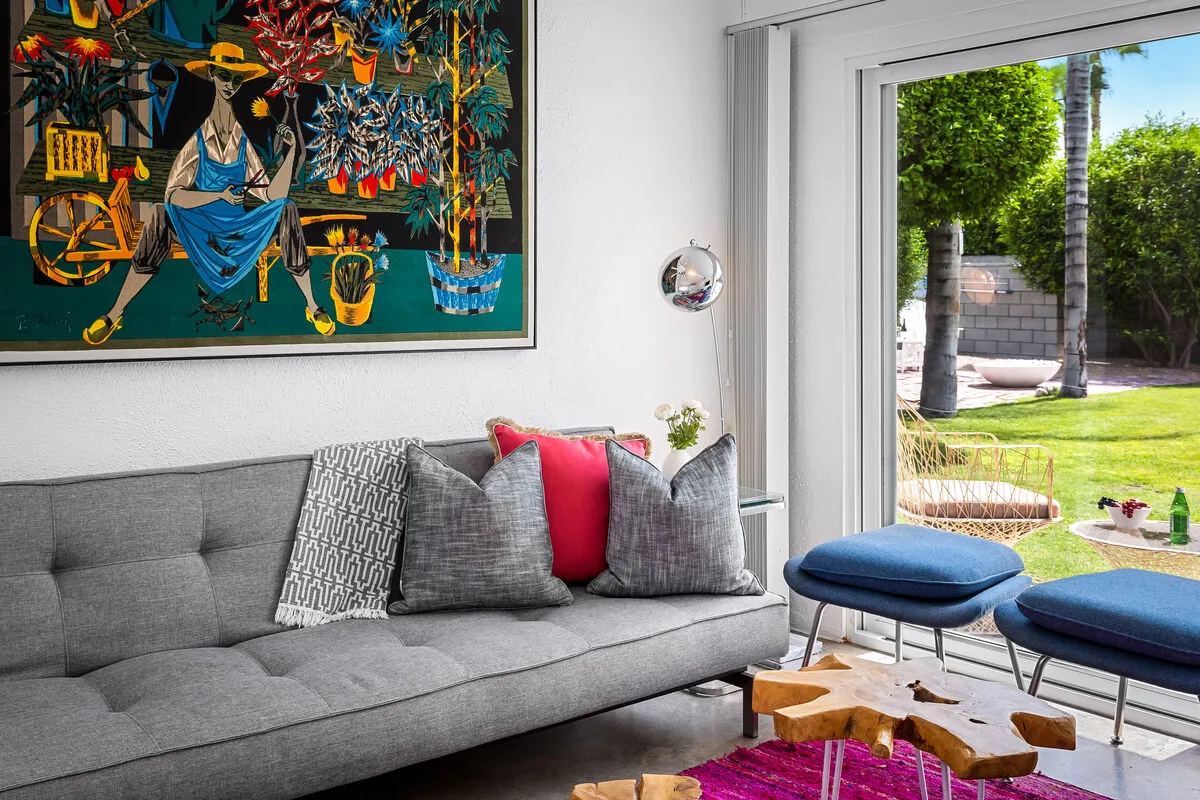 A living room with gray seating beside a large window overlooking a garden.