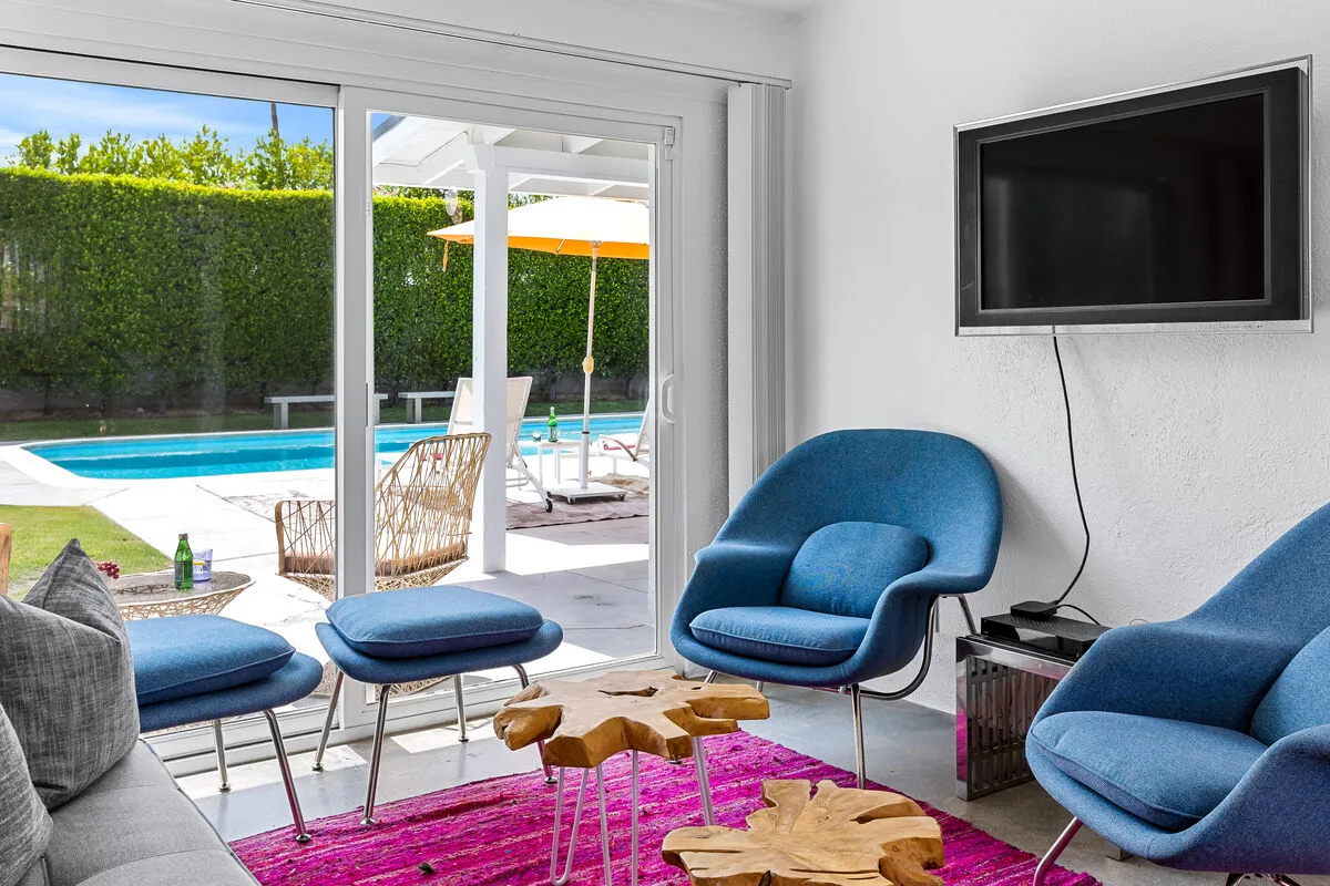 A bright living room with blue seating and sliding glass doors overlooking a pool.