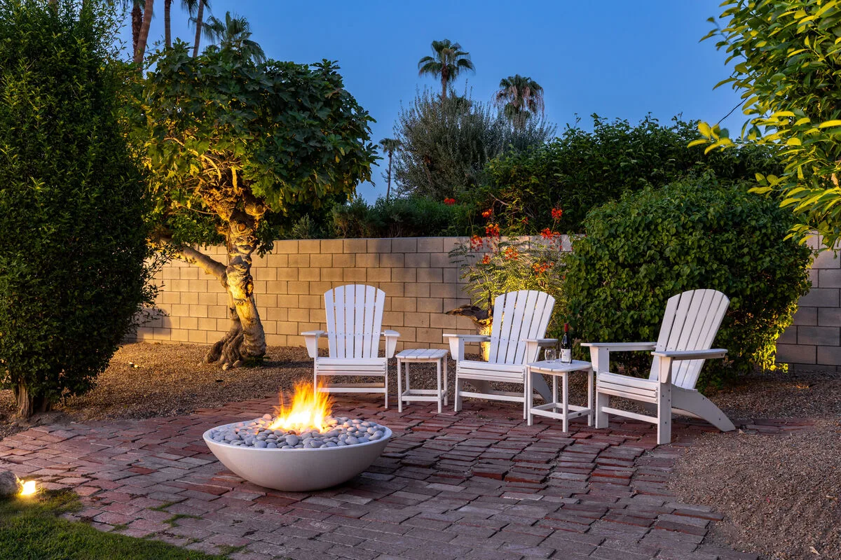 An outdoor patio with white seating arranged around a lit fire bowl.