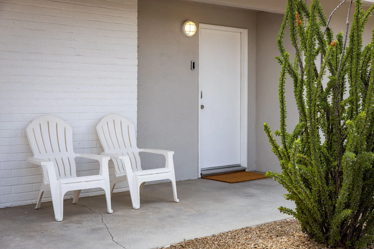 A covered entry porch with white seating beside a closed door.