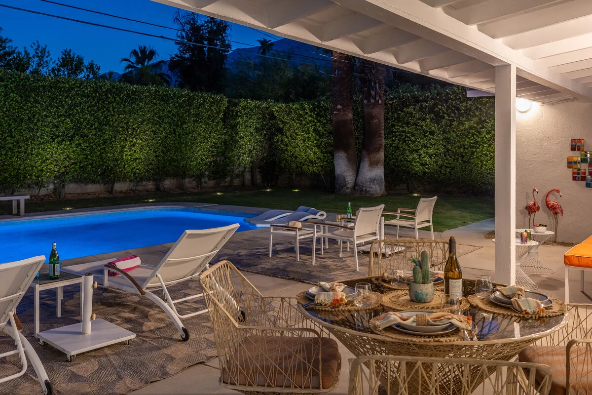 An outdoor patio with seating overlooks a swimming pool and garden hedge.