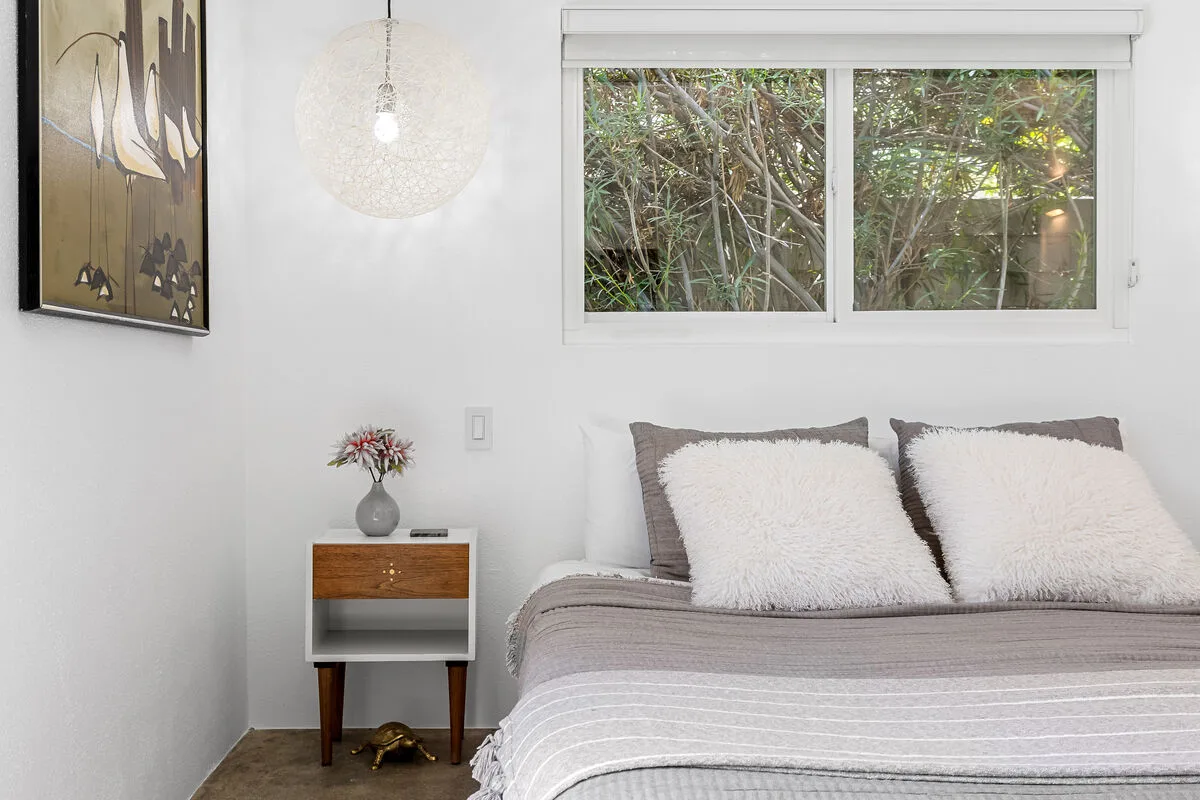 A bedroom with a neatly made bed and a window overlooking greenery.