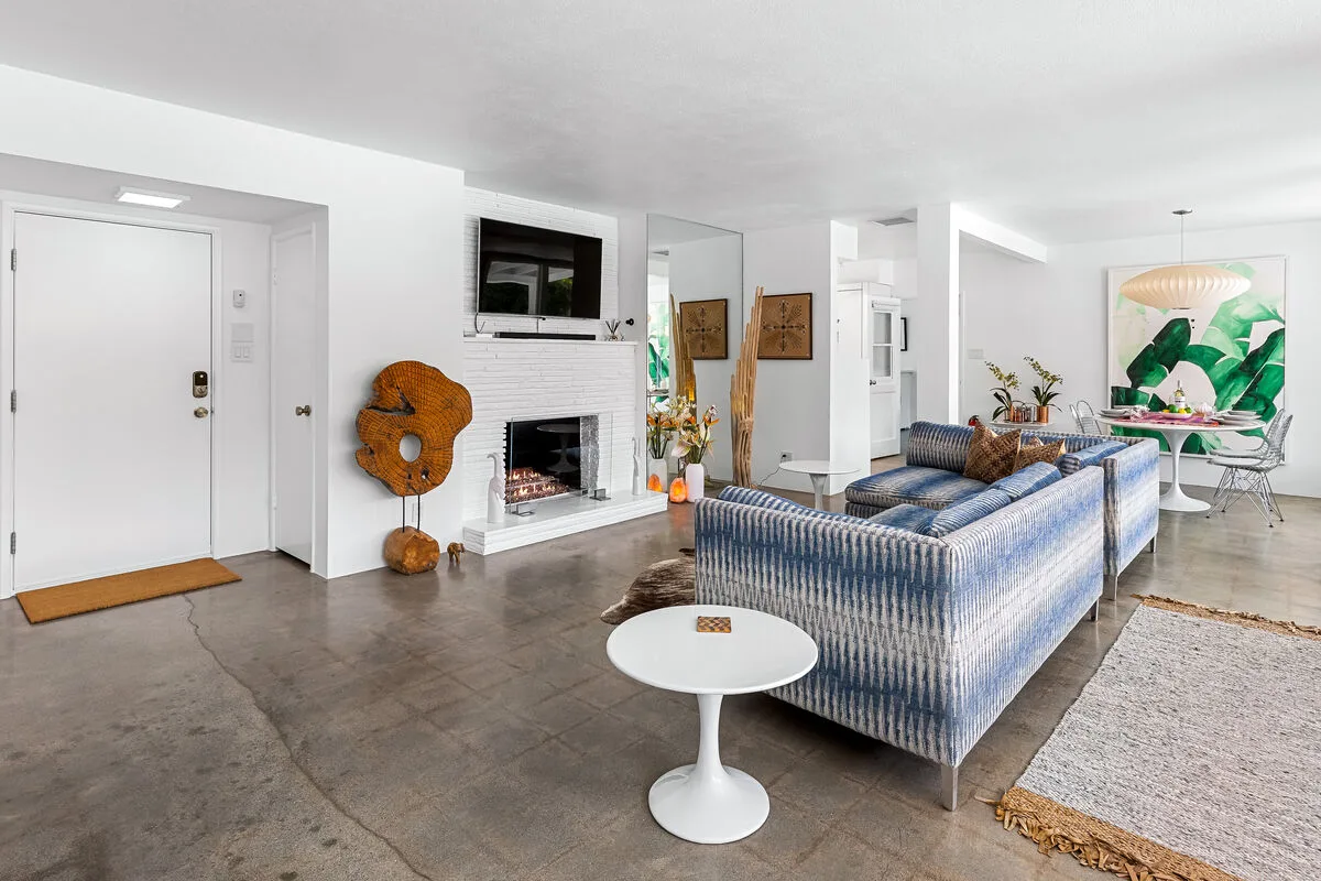 A bright living room with blue seating, a fireplace, and a round white table.