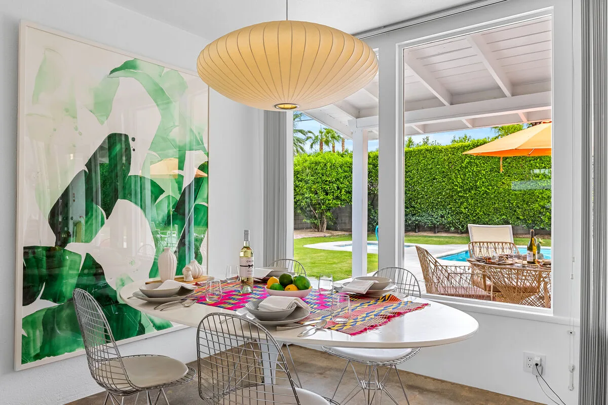 A dining area with a set table beside large windows overlooking a garden.