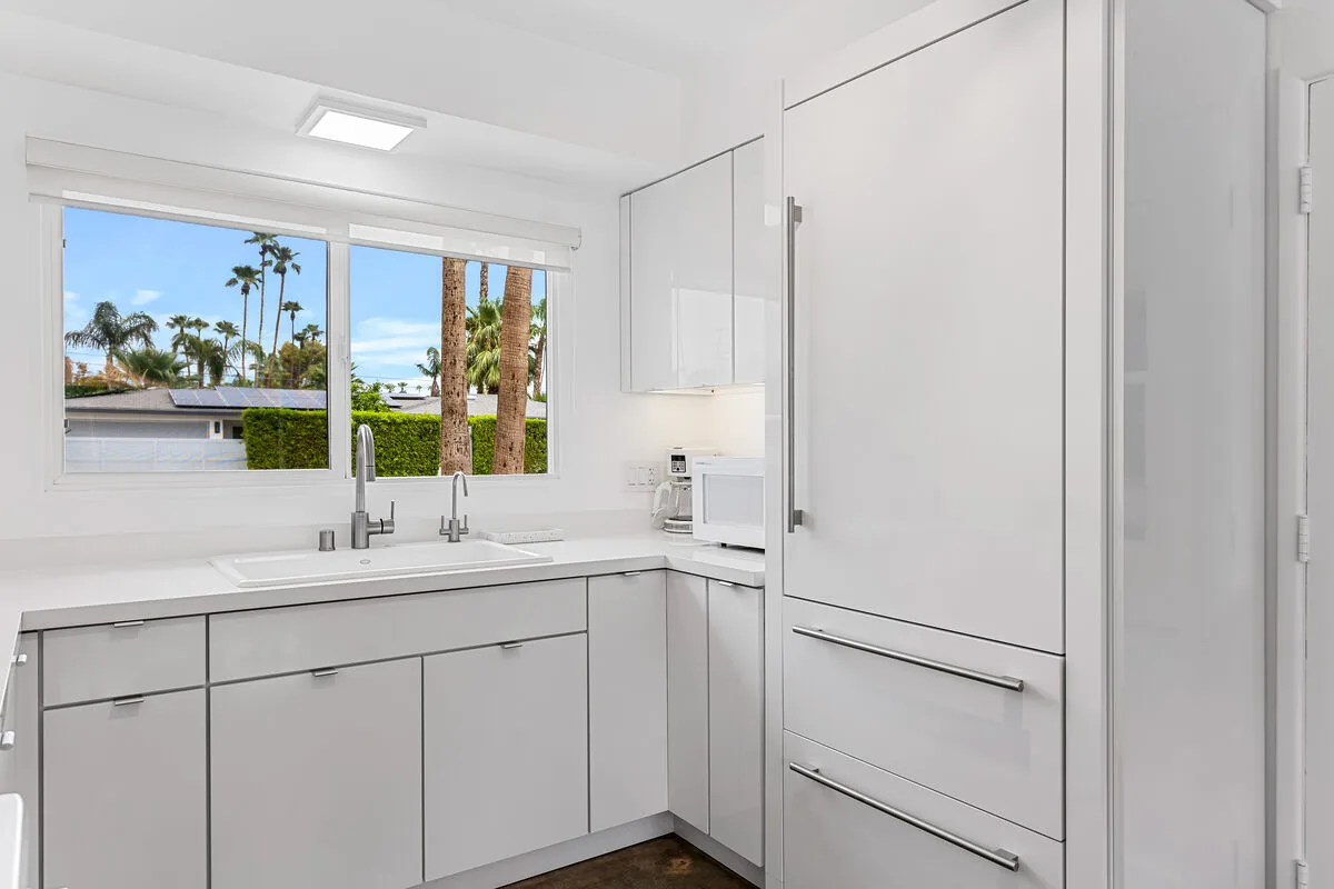 A bright white kitchen with a sink beneath a wide window.