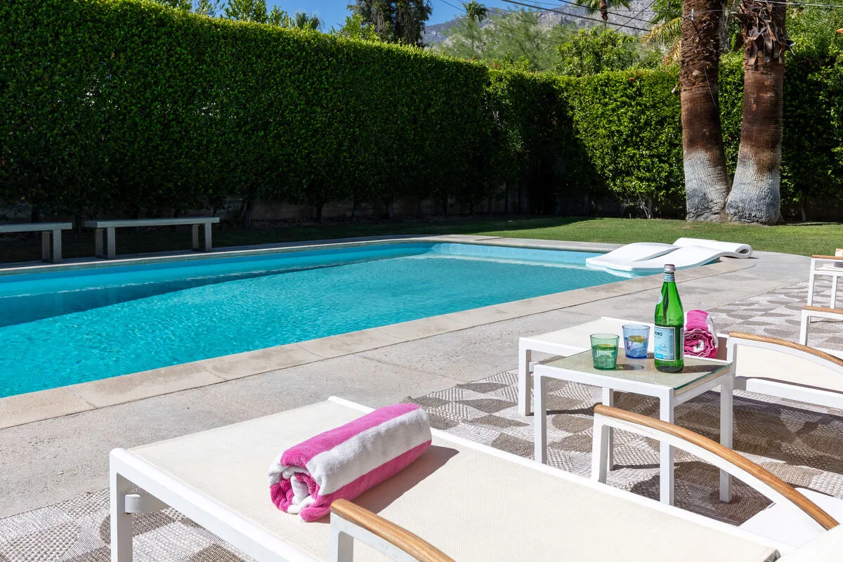 An outdoor swimming pool is surrounded by lounge chairs and greenery.