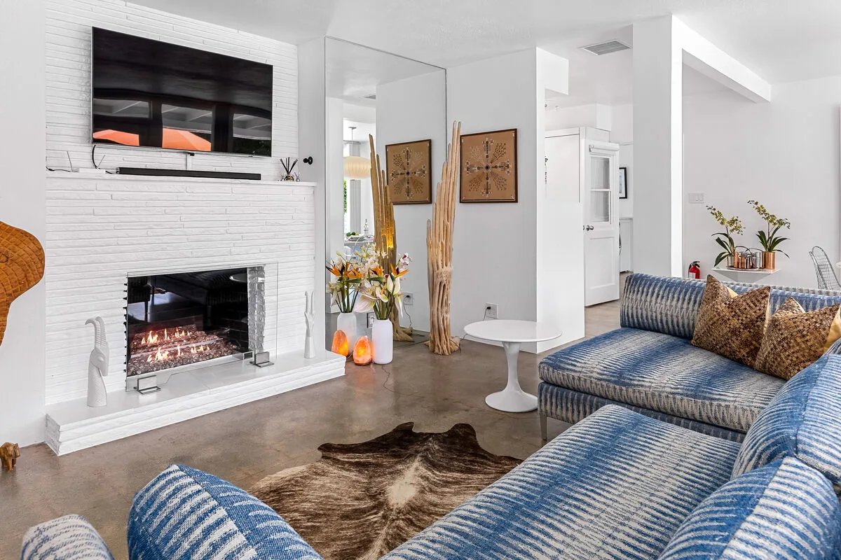 A bright living room with a fireplace, television, and blue patterned seating.