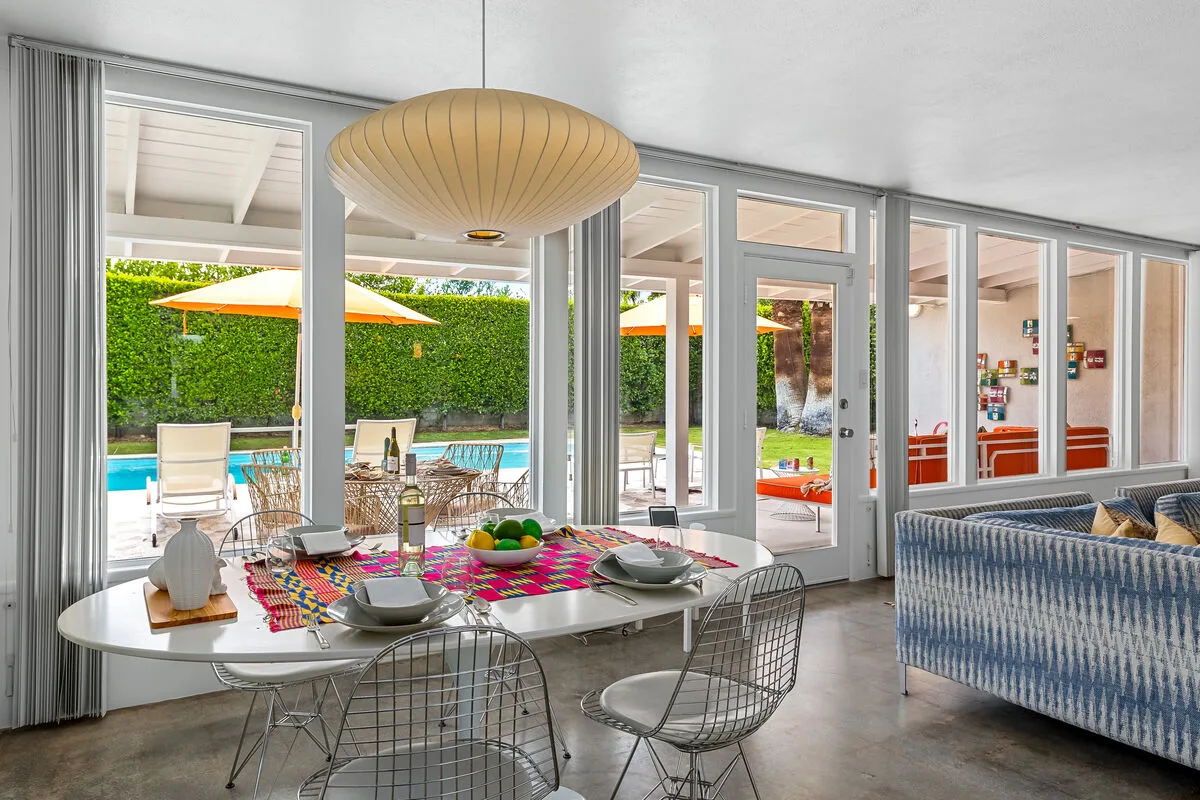 A bright dining area opens onto a poolside patio, with a table set for a meal.
