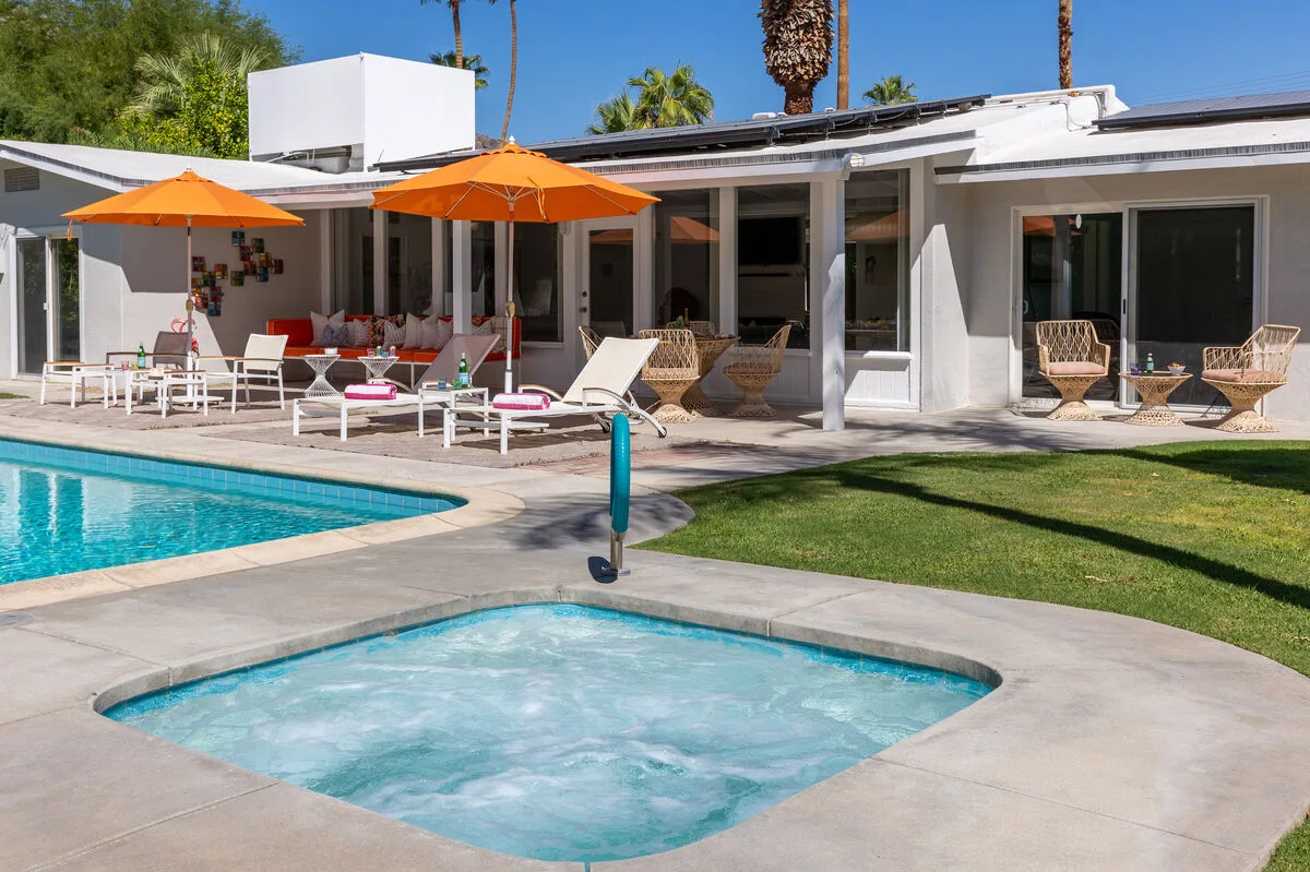 A swimming pool and bubbling spa sit beside a patio with orange umbrellas.