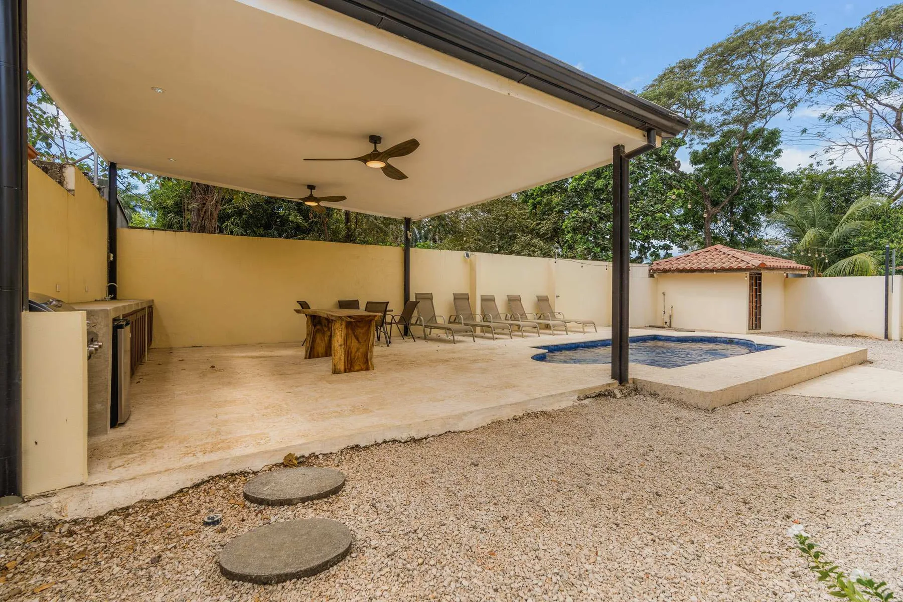 A covered outdoor patio has a dining table, lounge seating, and a small pool.