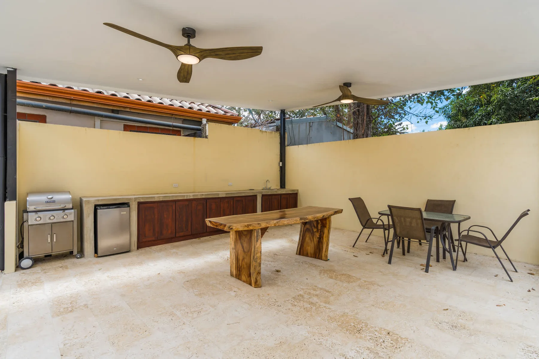 A covered outdoor dining area with a long wooden table and a built-in counter.