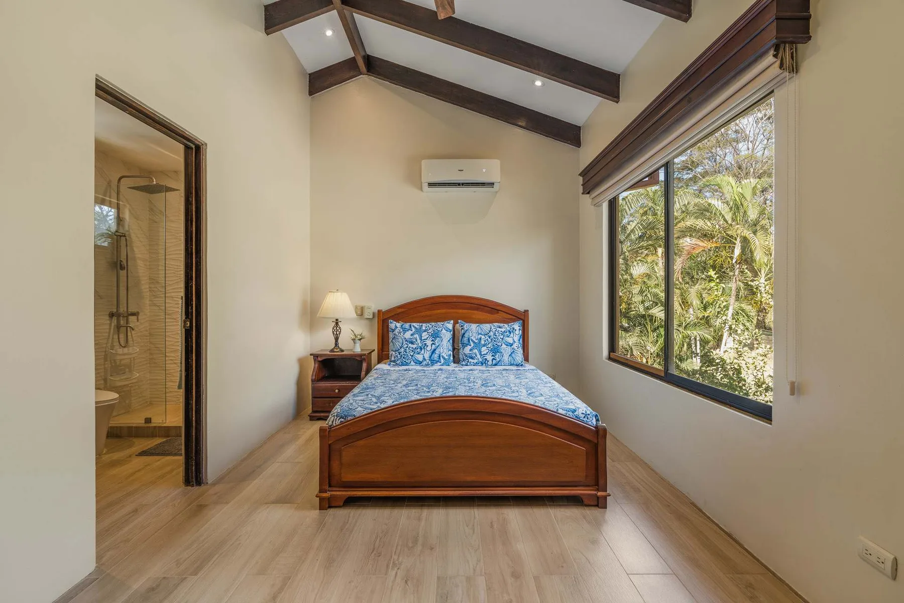 A bedroom with a wooden bed beneath exposed ceiling beams, beside a large window.