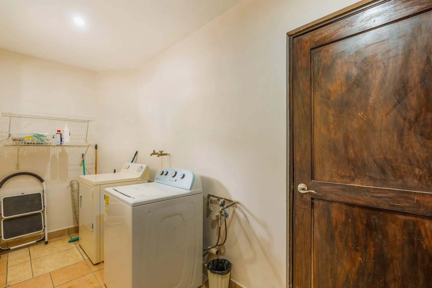 A laundry room with a washing machine, dryer, and wooden door.