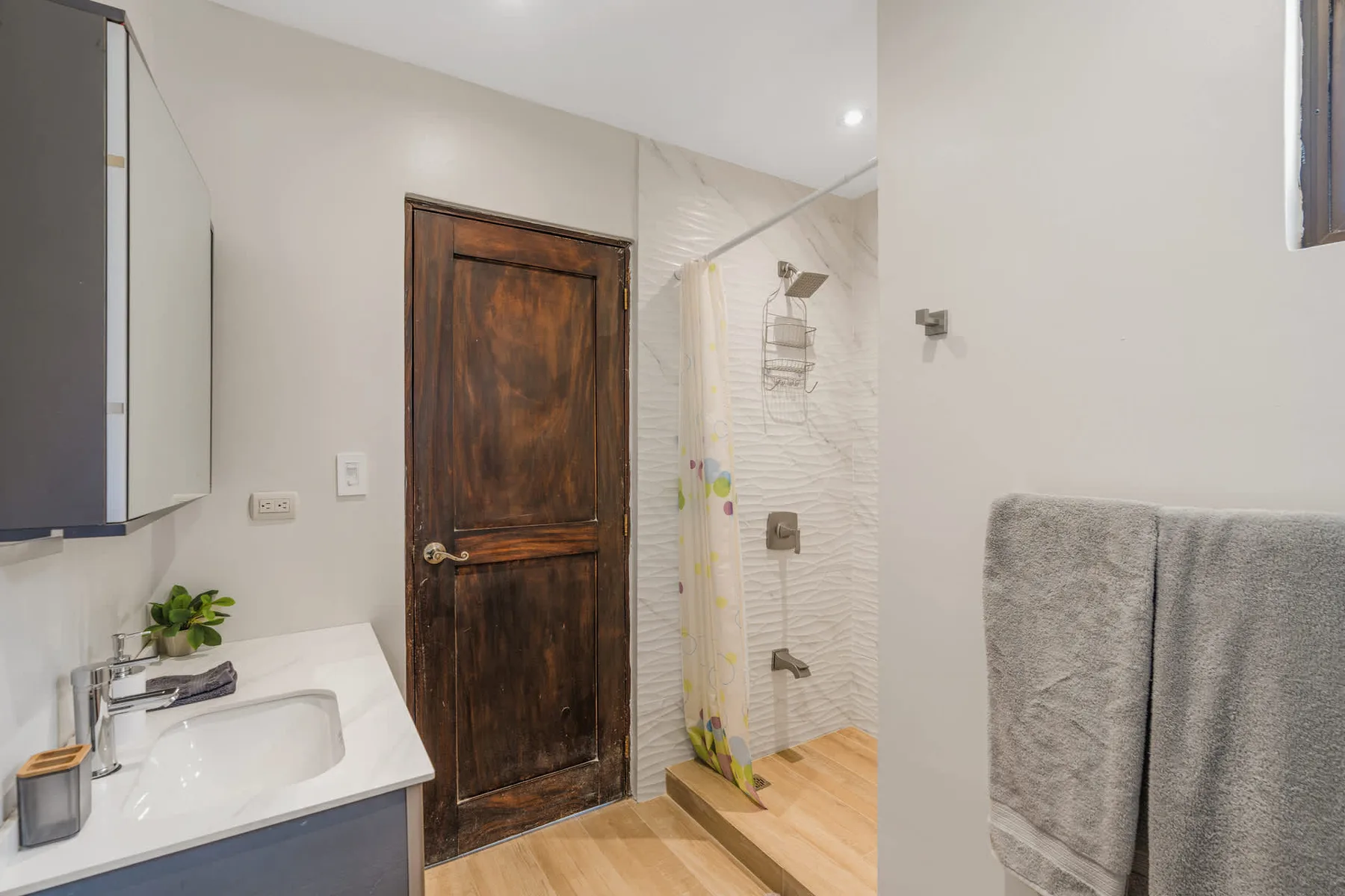 A bathroom with a sink, wooden door, and shower.