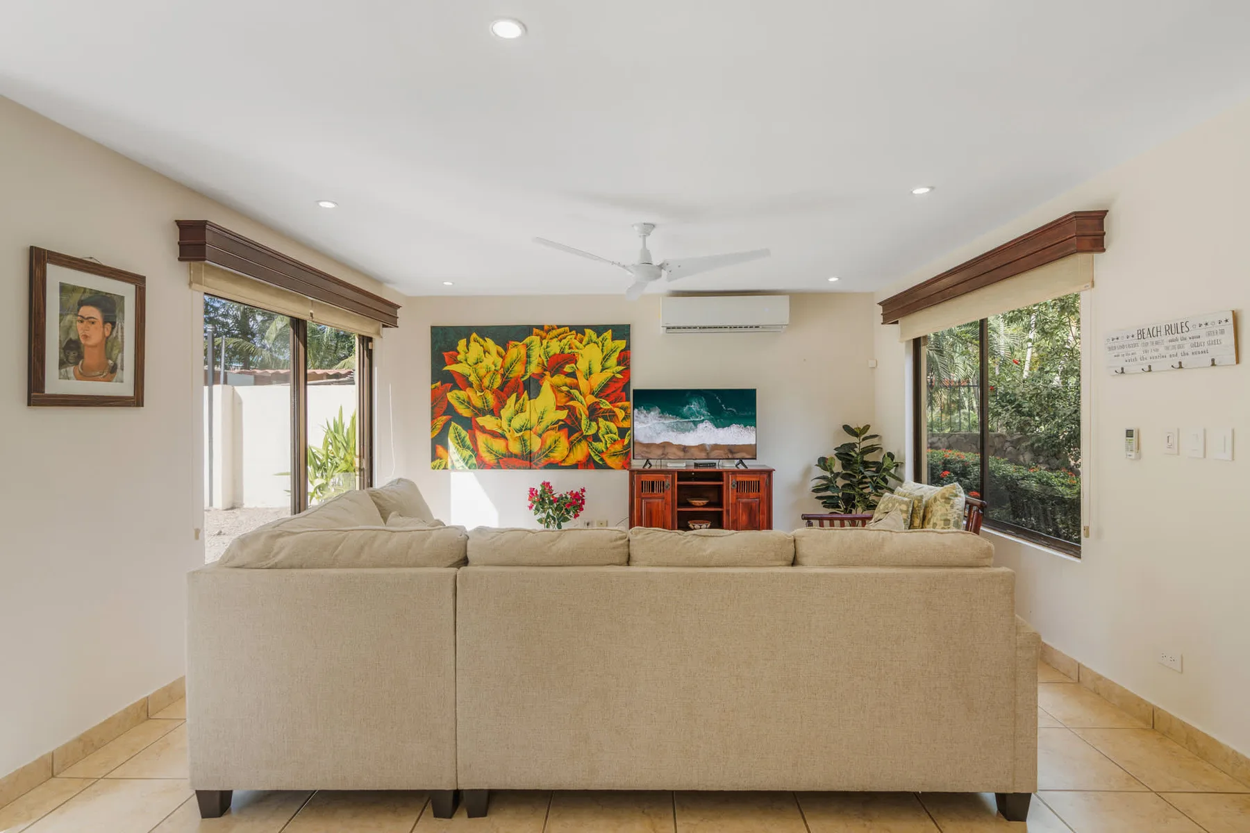 A bright living room with a beige sofa facing a television and colorful artwork.